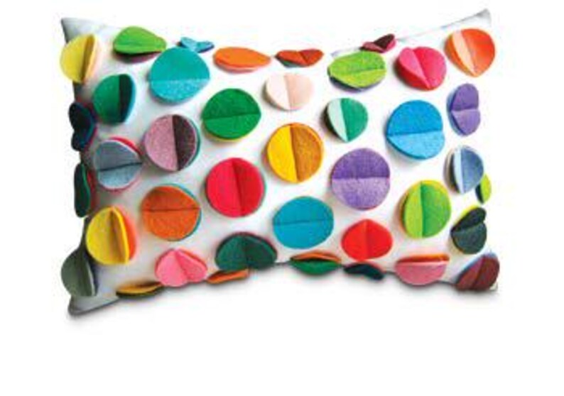 K&ouml;nnte beinhalten: Ein wei&szlig;es rechteckiges Kissen mit bunten Filzkreisen, die auf die Vorderseite gen&auml;ht sind. Die Kreise sind in verschiedenen Schattierungen von Rot, Orange, Gelb, Gr&uuml;n, Blau, Lila und Rosa.