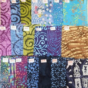 May include: A collection of twenty fabric swatches with various batik patterns. The swatches feature a range of colors, including purple, blue, green, and brown. Each swatch is labeled with a "D" followed by a number.