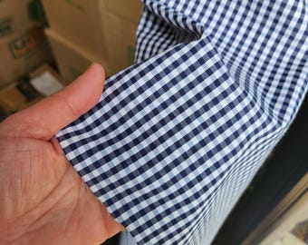 May include: Close-up of a white and navy blue gingham fabric. The fabric has a small checkered pattern.