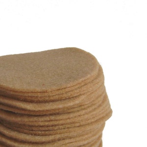 Puede incluir: Una pila de círculos de fieltro marrón, cada uno de aproximadamente 10 cm de diámetro, están apilados uno encima del otro. El fieltro es de color marrón claro y tiene una textura suave y peluda.