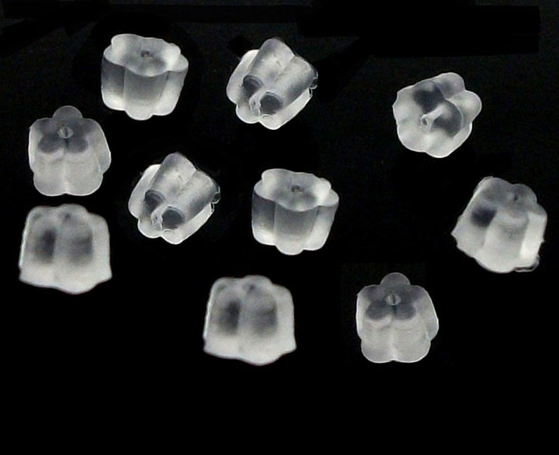 May include: A close-up of a group of clear silicone earring backs. The backs are shaped like a flower with a small hole in the center.
