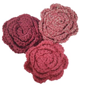 May include: Three crocheted rose flowers in shades of pink. The flowers are made with a soft, textured yarn and have a delicate, feminine look.