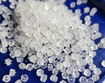 May include: A collection of small, translucent, flower-shaped earring backs made of soft silicone. These tiny, clear, petal-patterned components are scattered across a smooth, deep blue surface, highlighting their distinct floral shape and texture.