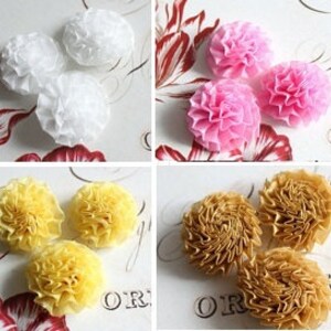 Puede incluir: Cuatro conjuntos de flores decorativas de papel en blanco, rosa, amarillo y dorado. Cada conjunto contiene tres flores con un diseño rizado y en capas. Las flores están dispuestas sobre una superficie estampada con estética vintage.