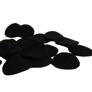 May include: A collection of black, oval-shaped felt pads, scattered against a white background. The pads have a slightly textured surface and are of varying sizes. They appear to be new and unused.