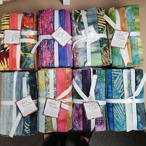 May include: A selection of fabric bundles, each tied with a white ribbon and a tag. The fabrics showcase diverse, colourful patterns, including batik designs in red, blue, green, and yellow. The tags read "Fabric Bundle".