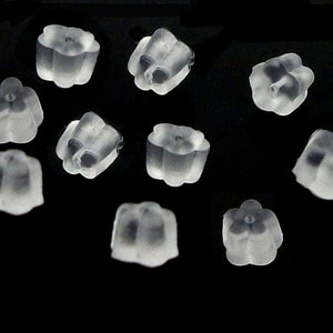 May include: A collection of nine small, clear, translucent silicone earring backs. Each piece features a flower-shaped design with a central hole for securing earring posts. The earring backs are arranged in a scattered pattern against a black background.