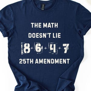 May include: Navy blue t-shirt with white text: "THE MATH DOESN'T LIE" and the equation "8 + 6 + 4 + 7" below it. The words "25TH AMENDMENT" are printed below the equation. The shirt is folded.