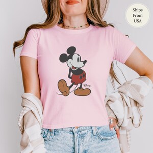 Puede incluir: Camiseta rosa claro con un dibujo de Mickey Mouse. El personaje de dibujos animados est&aacute; representado en negro, rojo y marr&oacute;n, con el logotipo de Disney debajo. La camiseta de manga corta est&aacute; hecha de un material suave.