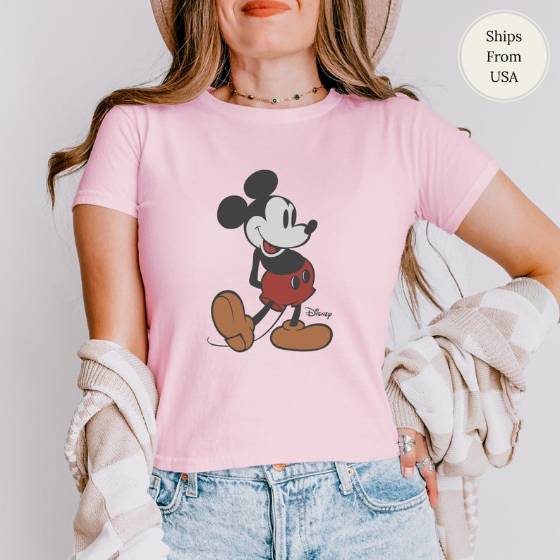 Puede incluir: Camiseta rosa claro con un dibujo de Mickey Mouse. El personaje de dibujos animados est&aacute; representado en negro, rojo y marr&oacute;n, con el logotipo de Disney debajo. La camiseta de manga corta est&aacute; hecha de un material suave.