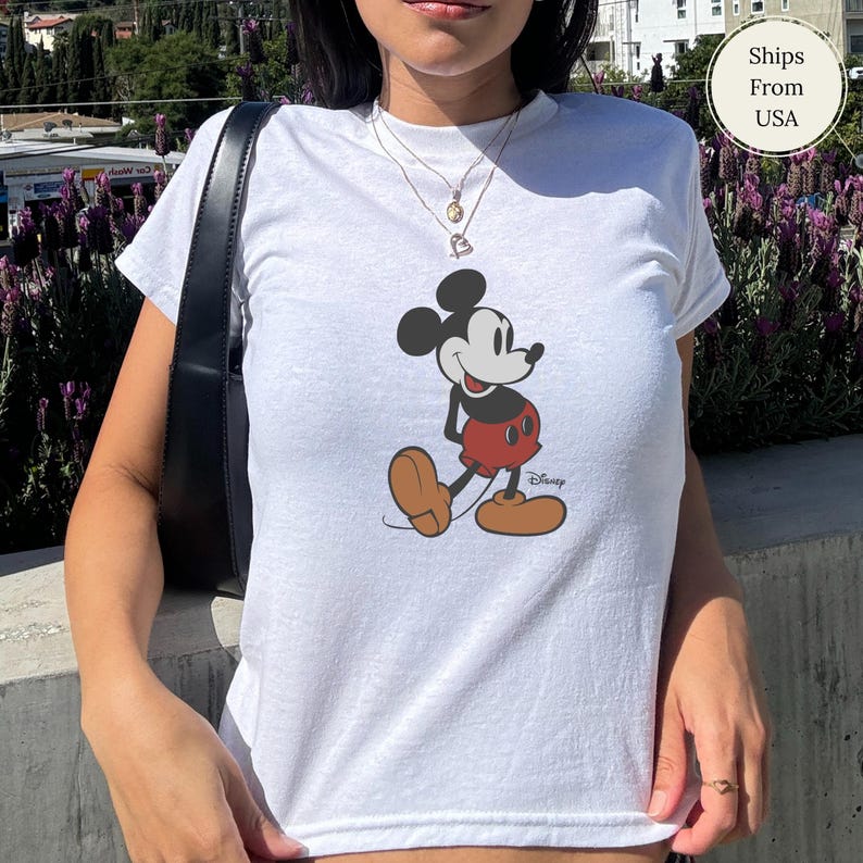 Puede incluir: Camiseta blanca con un gr&aacute;fico de Mickey Mouse en negro, rojo y marr&oacute;n. El logotipo de Disney est&aacute; impreso debajo del personaje. La camiseta tiene mangas cortas y cuello redondo.