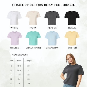 Puede incluir: Camiseta Comfort Colors Boxy Tee 3023CL en ocho colores: blanco, marfil, pimienta, negro, orqu&iacute;dea, menta tiza, chambray y mantequilla. Una tabla de tallas muestra medidas de ancho y largo en pulgadas para tallas S a 2XL, junto a una camiseta color pimienta.