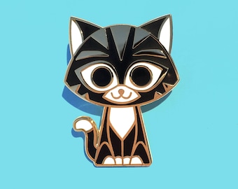May include: Gold-tone enamel pin featuring a cartoon black and white cat with large eyes. The cat has a black stripe across its face and a white chest.