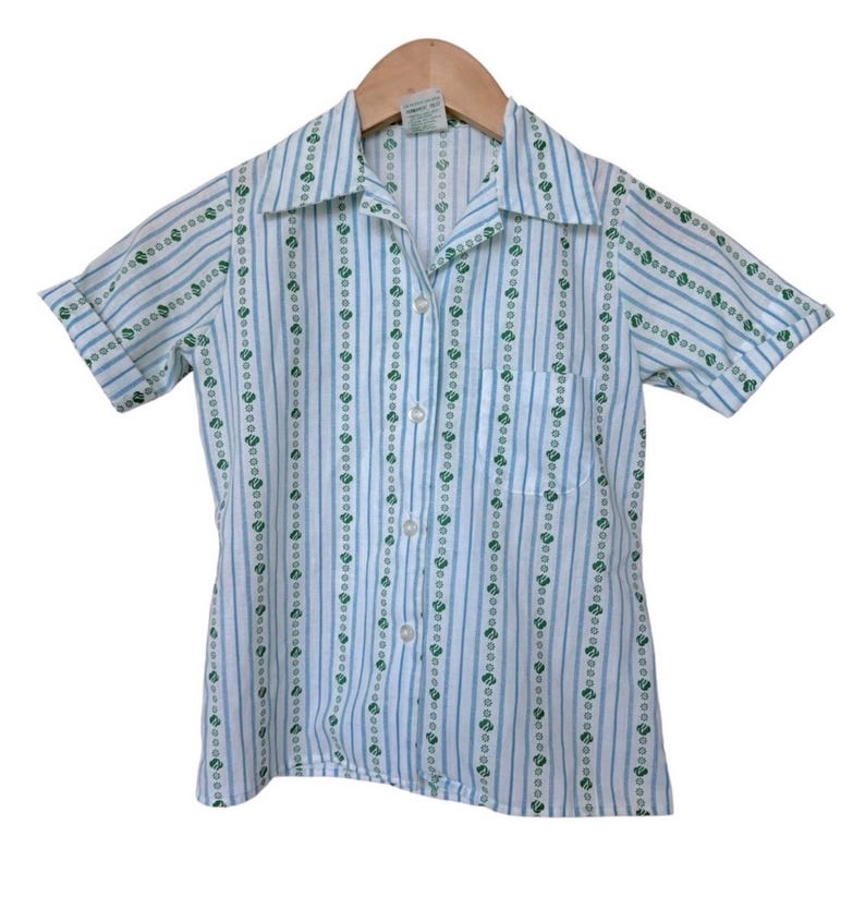 May include: A short-sleeved shirt with a white and blue striped design, featuring green heart-shaped patterns. The shirt has a collared neckline, a single chest pocket, and is fastened with buttons. The shirt is suitable for casual wear.