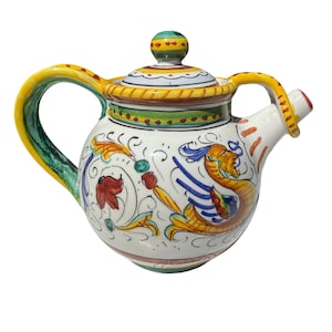May include: A hand-painted ceramic teapot with a lid and spout. The teapot features a white base with colorful floral and mythical creature designs. The handle and spout are yellow, and the lid has a green and yellow knob.