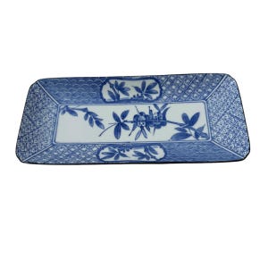 May include: A rectangular ceramic serving tray featuring a white base with blue hand-painted botanical illustrations of bamboo stalks and leaves. The border displays a mix of geometric lattice patterns and wave motifs in blue and white.