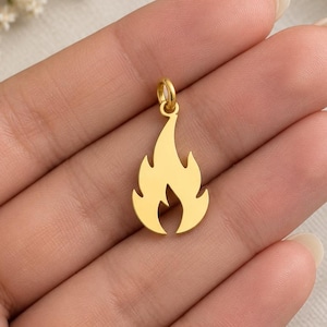 May include: A gold-colored metal pendant shaped like a stylized flame. The pendant features a smooth, solid surface with a small circular jump ring attached to the top for hanging. The design is symmetrical with pointed edges representing a fire.