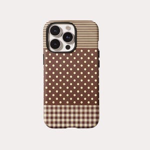 Puede incluir: Una funda para smartphone con un diseño de patrón en tres partes. La sección superior tiene rayas horizontales color crema y marrón, la sección central es marrón con lunares crema y la sección inferior presenta un patrón de cuadros vichy.