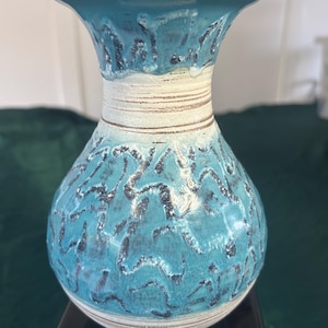 May include: A ceramic vase featuring a bulbous body and a flared rim. The surface displays a vibrant turquoise glaze with a textured, dark blue, organic pattern. The neck and base are accented with horizontal white bands and subtle brown detailing.