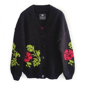 Puede incluir: Cárdigan negro con cuello en V y cierre de botones. El suéter de punto presenta un diseño floral en rojo y verde en las mangas y el frente. Una etiqueta con texto es visible en la parte superior de la espalda.