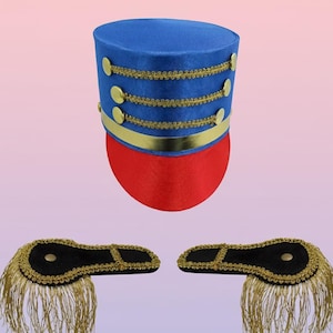 May include: A blue and red toy soldier hat with gold trim and buttons. Two black epaulettes with gold fringe are also shown. The hat has a cylindrical shape with a red base and a blue top. The epaulettes are black with gold trim and fringe.
