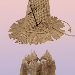 Może przedstawiać: Rustykalny zestaw kapelusza i kołnierza stracha na wróble wykonany z juty. Kapelusz ma stożkowy kształt z szerokim, postrzępionym rondem i jest przeszyty czarną nicią. Kołnierz jest również wykonany z juty z postrzępioną krawędzią. Akcesorium kostiumu na Halloween.