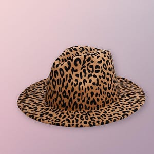 May include: A fedora hat with a leopard print pattern in shades of brown and black. The hat has a wide brim and a structured crown. The hat is a stylish accessory.