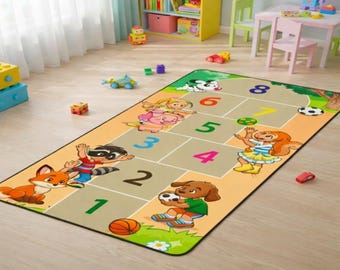 May include: A rectangular children's play rug featuring a hopscotch design with numbers 1-8. The rug has cartoon illustrations of animals and children playing with balls. The rug is beige with a black border.