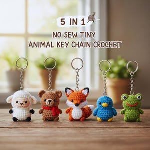 Puede incluir: Cinco llaveros de animales de ganchillo: una oveja blanca, un oso marrón con una bufanda roja, un zorro naranja, un pájaro azul y una rana verde. Cada llavero tiene un anillo y una cadena plateados. El texto dice "5 en 1".