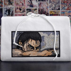 May include: White hoodie with a detailed embroidered image of an anime character. The character has black hair, blue eyes, and a determined expression. The hoodie has a white drawstring.