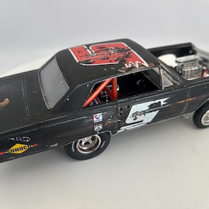 May include: A black model race car with the number 5 in white on the side and roof. The car has a distressed paint finish, a roll cage, and the word "SUNOCO" on the side. The engine is visible.