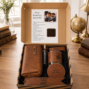 May include: A brown leather gift set in a cardboard box containing a zippered pouch, a glass bottle with a leather sleeve featuring an eagle and flag design, a round coaster engraved with THE BEST DAD EVER, and a bookmark with I LOVE YOU DAD.