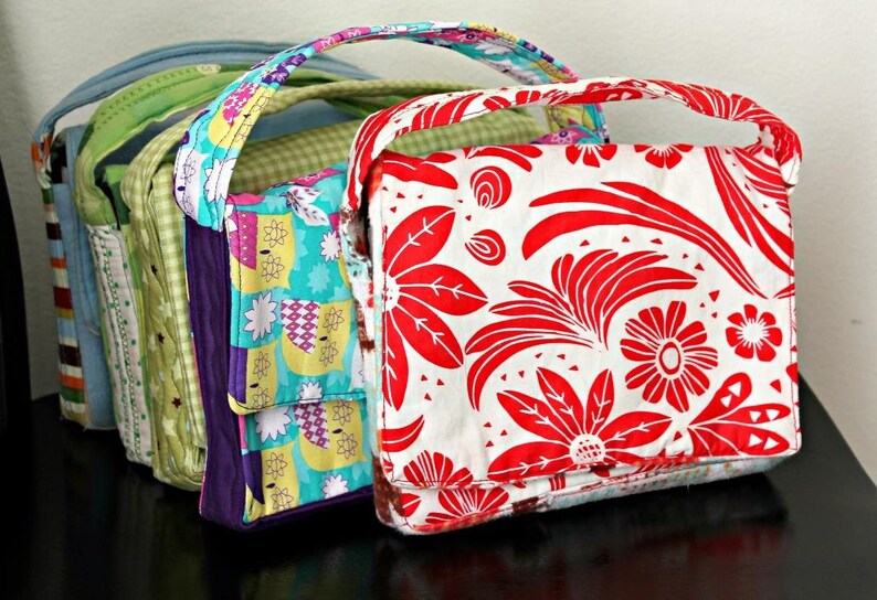 May include: A collection of colorful, handmade fabric tote bags. The bags feature various patterns, including floral, geometric, and patchwork designs. Each bag has a matching handle and a rectangular shape, perfect for carrying essentials. The bags are displayed in a row, showcasing their unique designs.