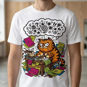 Op de afbeelding: Wit t-shirt met een cartoon illustratie van een oranje en zwart gestreepte kat die er gestrest uitziet aan een bureau. De kat is omringd door papieren en een koffiekopje, met een denkbel boven zijn hoofd vol symbolen.