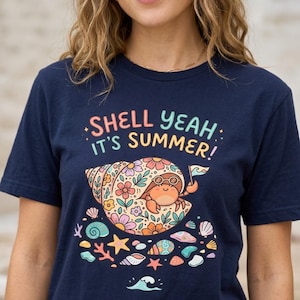 Puede incluir: Camiseta azul marino con un gráfico colorido de un cangrejo ermitaño en una concha, con gafas de sol y sosteniendo una bandera. El texto "SHELL YEAH IT'S SUMMER!" está encima del gráfico. El diseño incluye flores, conchas y estrellas de mar.