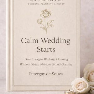 Op de afbeelding: Een crème hardcover boek getiteld "Calm Wedding Starts" uit de Ts & Is Collection Wedding Planning Library. Het boek heeft een bloemenillustratie en de naam van de auteur, Petergay de Souza. Trouwringen en rozen staan op de achtergrond.