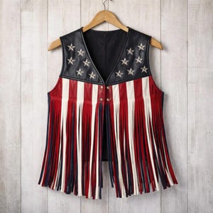 Front view of American flag fringe leather vest on hanger. Patriotic women’s leather vest featuring star-studded black leather, red and white stripes, and long western fringe. Festival and biker style vest inspired by USA Independence Day fashion.