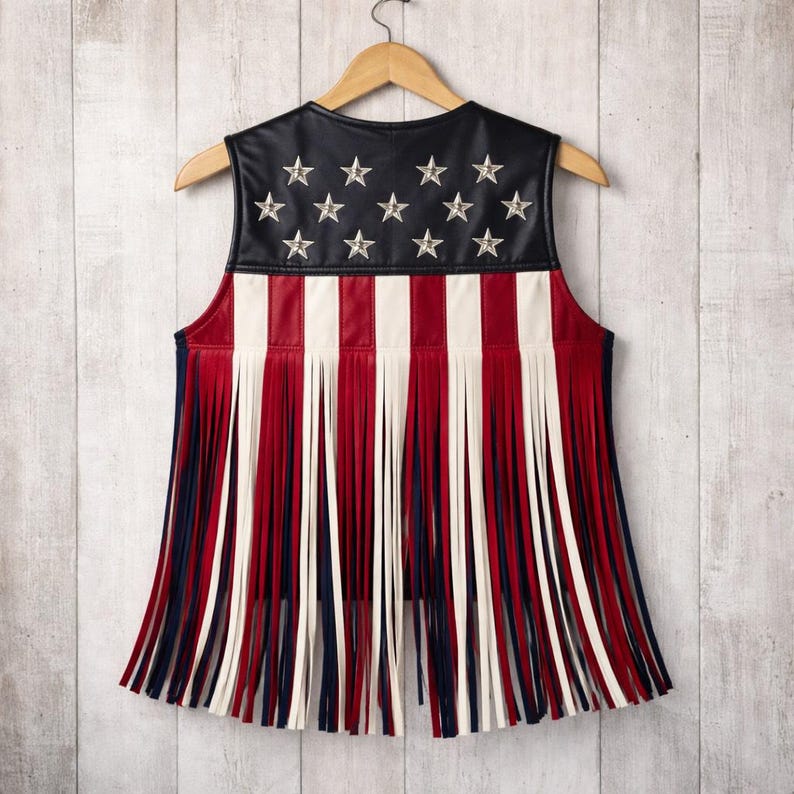 Back view of American flag fringe leather vest displayed on a wooden hanger. Patriotic women’s vest with black leather top, silver star details, red white blue stripes, and long western fringe. Handmade USA inspired leather vest for 4th of July outfits.