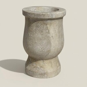 May include: A weathered, gray stone vase with a bulbous body and a wide, circular opening. The vase has a textured surface and a slightly flared rim. The base is a smaller, rounded shape. The overall design is simple and elegant.