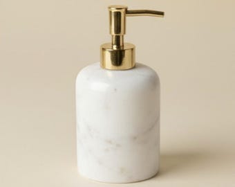 May include: A white marble soap dispenser with a gold-coloured pump. The dispenser has a rounded shape and a polished finish. The gold pump is positioned at the top of the dispenser.