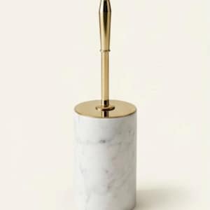 Op de afbeelding: Een witte marmeren toiletborstelhouder met een goudkleurige handgreep en voet. De cilindrische houder heeft grijze adering en de borstelsteel is bekroond met een afgeronde, goudkleurige knop. Modern en minimalistisch design.