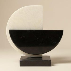 May include: Abstract sculpture featuring a semi-circular white marble form juxtaposed with a black marble half-circle. The sculpture rests on a square black marble base, showcasing a modern, minimalist design.