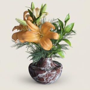 May include: A floral arrangement featuring orange lilies and green foliage in a decorative vase. The vase has a dark red and white marbled pattern. The lilies are in full bloom, with several buds and leaves adding to the arrangement's natural aesthetic.