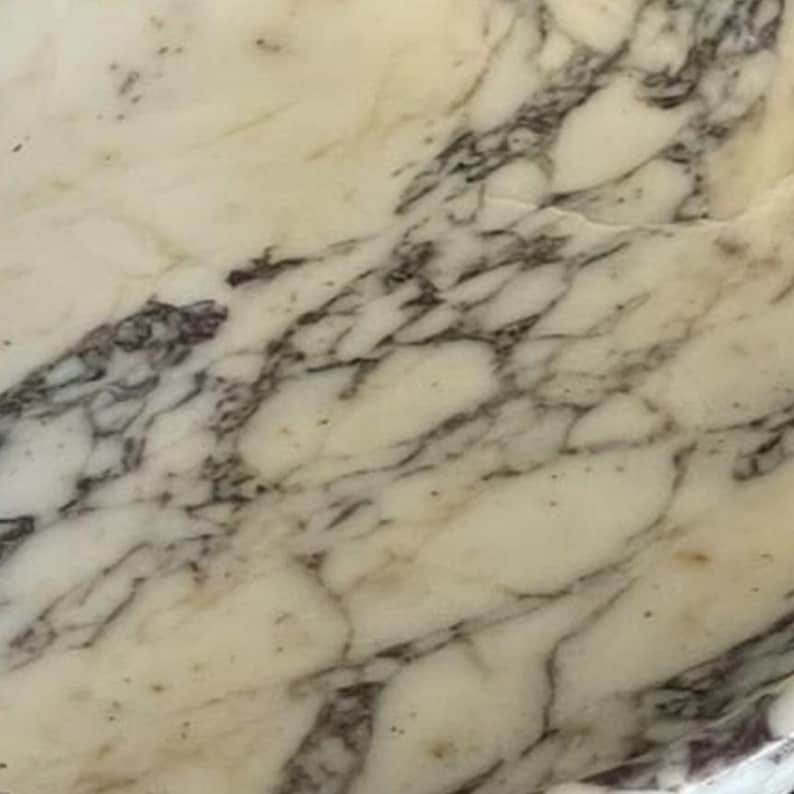 Puede incluir: Primer plano de una superficie de m&aacute;rmol crema con vetas grises oscuras. El patr&oacute;n de piedra natural presenta l&iacute;neas y formas irregulares, creando una textura &uacute;nica. Ideal para la decoraci&oacute;n del hogar y proyectos de dise&ntilde;o.