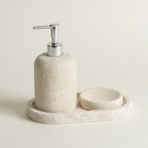 May include: A beige stone soap dispenser with a silver pump, a small soap dish, and a tray. The set is made of a textured stone material. The soap dispenser and soap dish sit on an oval tray.
