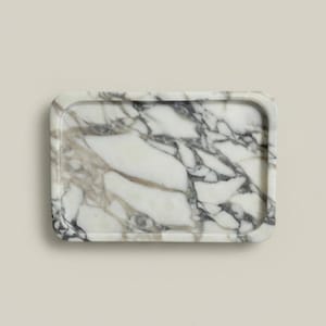 May include: Rectangular marble tray with rounded corners. The tray features a white base with gray and brown veining throughout. The tray is a decorative item.
