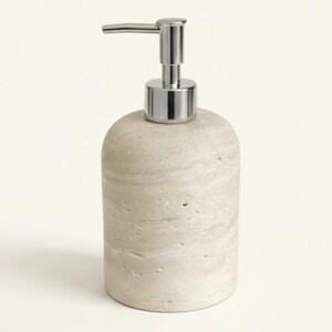 May include: A beige stone soap dispenser with a silver pump. The dispenser has a cylindrical body with a rounded top and a textured surface. The pump is made of shiny metal.
