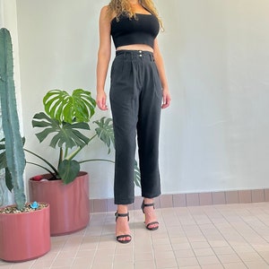 May include: A person wearing black pants with a high waist and a black crop top. The pants have a straight leg and are made of a lightweight fabric. The person is wearing black heeled sandals.