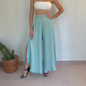 May include: A white tube top paired with high-waisted, wide-leg pants in a light blue hue. The pants feature side slits and a contrasting light blue trim. Black sandals complete the outfit, creating a summery, casual look.
