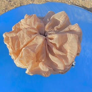 May include: A large, beige, sheer hair scrunchie with a grid pattern. The scrunchie is made of a soft, lightweight fabric and is perfect for adding a touch of elegance to any hairstyle.